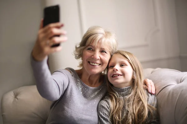 Smiling grandmother and grand daughter taking a selfie together on a sofa.