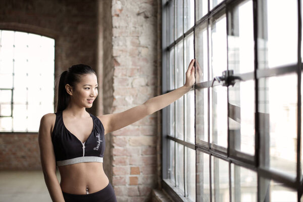 Beautiful young Asian woman  in sport outfit standing at the window looking out.