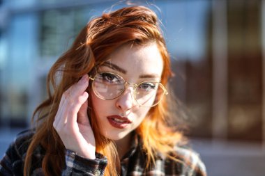 Kameraya bakarak gözlük olan kızıl saçlı kadın.