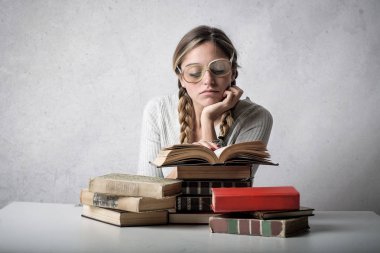 Kitap okuma ve bıkkın ve yorgun görünümlü gözlüklü sarışın genç kadın.