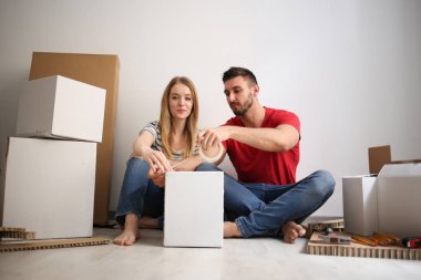 Kapalı yerde otururken bir kağıt kutu bandı ile kapanış genç mutlu çift.