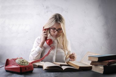 Gözlüklü sarışın kız ile eski bir telefon kitaplarını önünde arar.