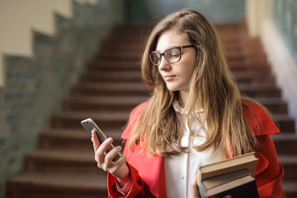 戴眼镜的年轻女子在大学走廊上检查她的智能手机 — 图库照片