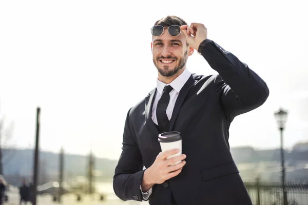 Young businessman with coffee to go smiling into the camera.