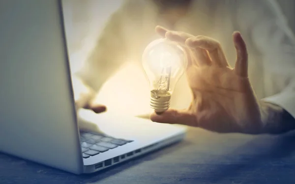 Hand with light bulb in front of a computer.