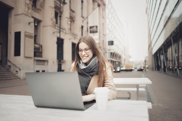 年轻快乐的女人坐在一个露台在秋季与她的笔记本电脑和微笑 — 图库照片