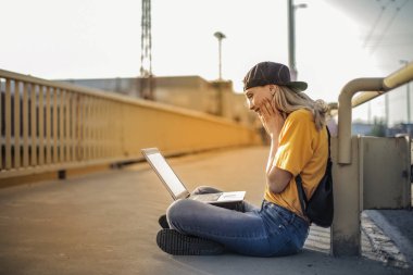 Bir köprü üzerinde oturan ve onu laptop kontrol Genç Sarışın genç.