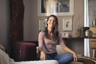 Evde zarif bir sandalyede oturan ve gülümseyen genç güzel kadın.