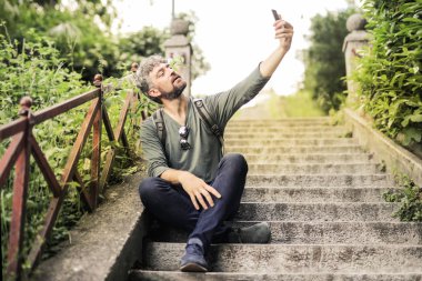 Bir merdiven şehirde oturan ve bir selfie alarak kıvırcık saçlı adam.