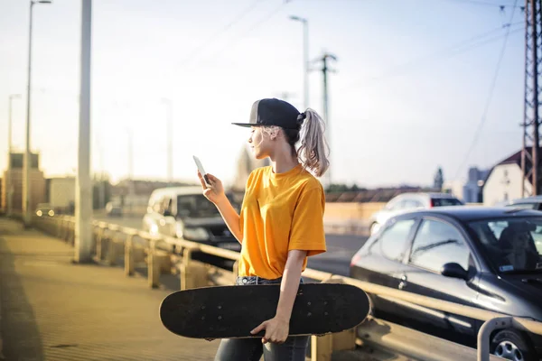 Young blonde teenager with baseball hat checking her smartphone in the city.