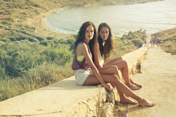 两位女性朋友坐在一条崎岖的公路上 背景是大海 — 图库照片