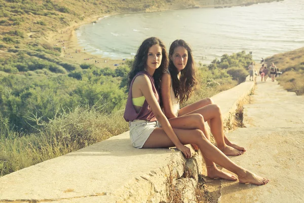 Duas Amigas Sentadas Uma Estrada Rochosa Com Mar Fundo — Fotografia de Stock