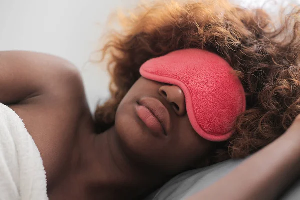 Young Afro woman sleeping in a pink sleeping mask.