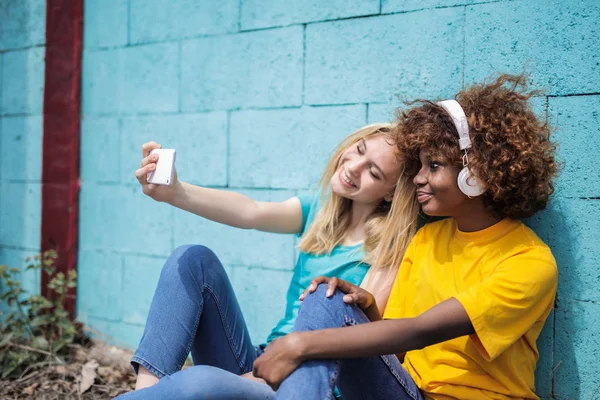 Dos Jóvenes Amigas Sentadas Junto Una Pared Azul Tomando Una —  Fotos de Stock