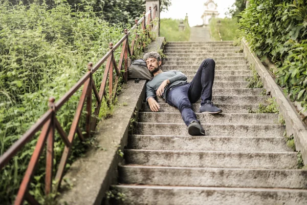 Kıvırcık Saçlı Adam Çantasını Şehirde Bir Merdiven Üzerinde Uyku — Stok fotoğraf