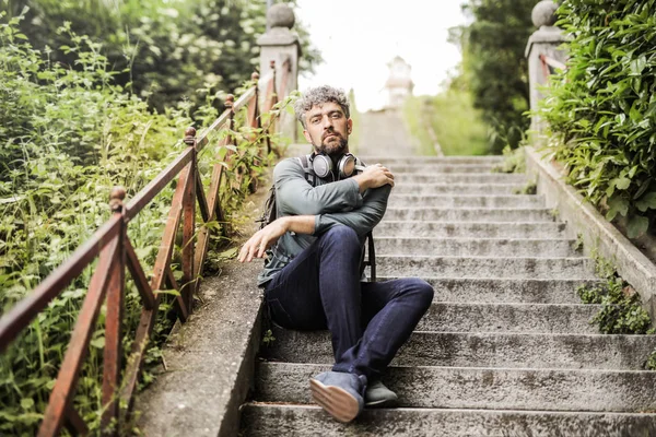 Bir merdiven şehirde oturan ve üzülmüş kulaklıklarla kıvırcık saçlı adam.