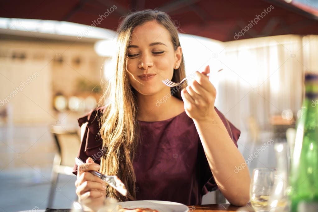 Young pretty woman having lunch on a terrace on a sunny day and smiling.