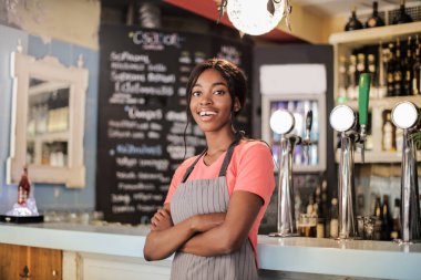 Genç güzel Afro kadın bar önünde duran ve gülümseyen garson olarak.