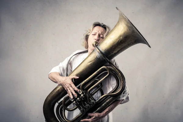 Senior woman playing tuba indoor.