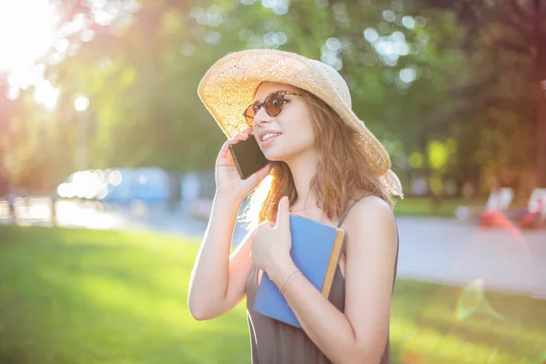 麦わら帽子と夏の日の公園で彼女のスマート フォンを屋外話サングラスを身に着けている若者 — ストック写真