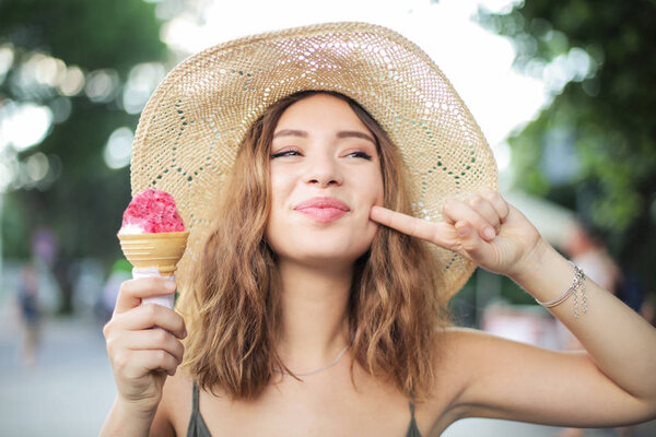 Молодой подросток в соломенной шляпе делает смешное лицо и ест мороженое в парке в летний день
.