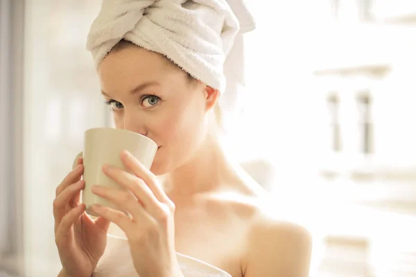 年轻漂亮的女人用毛巾在她的头上喝咖啡在早上 — 图库照片