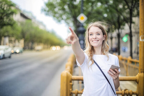 Happy young pretty blonde woman pointing out on the street.