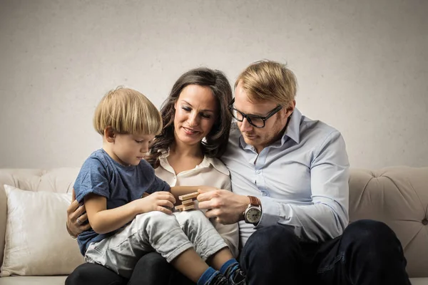 若い家族は屋内のソファーに座っている幼児と — ストック写真