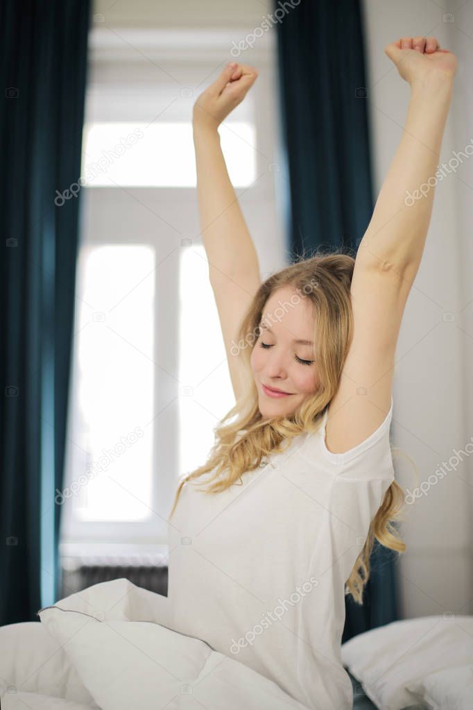 Young beautiful blonde woman waking up in her bed and stretching.