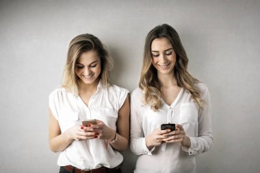 İki güzel genç kadın gülümseyerek ve onların smartphone kapalı kontrol beyaz gömlekli.