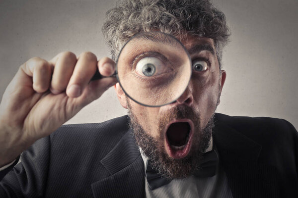 Curly-haired businessman with a magnifying glass looking surprised.