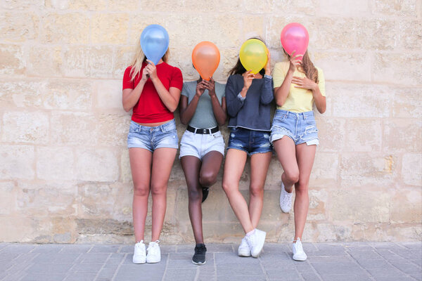 Group of female friends having fun and hiding their faces with air balloons.