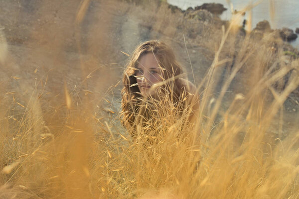 Beautiful young woman hiding on a meadow on a sunny day.