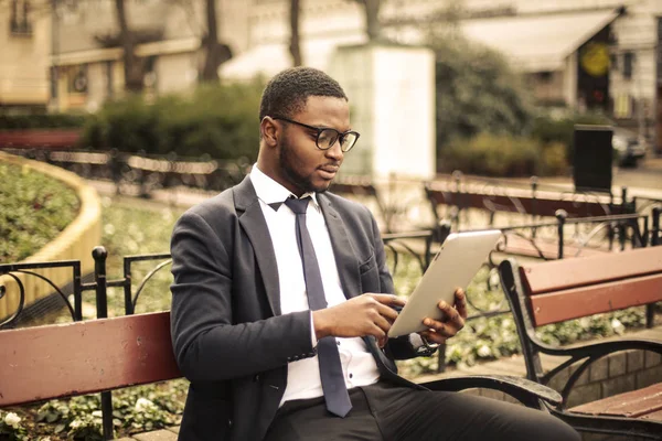 黑人非洲商人戴着眼镜坐在长椅上 在城里看报 — 图库照片
