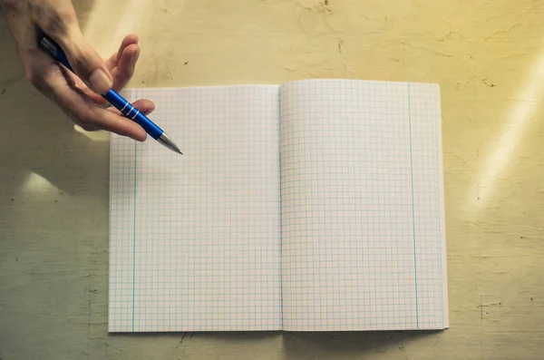 一只手拿着钢笔和一张空笔记本在桌子上 — 图库照片