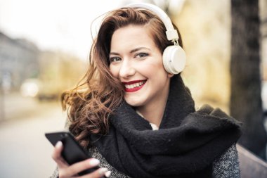 Gülümseyen ve onun smartphone denetlerken sokakta müzik dinlerken kulaklık ile zarif kadın.