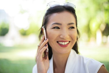 Onun smartphone üzerinde konuşmak ve güneşli bir günde açık gülümseyen Asyalı zarif kadın.
