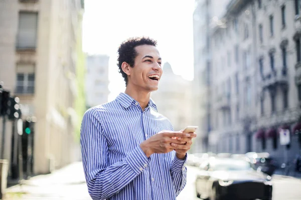 年轻自信的非洲人微笑着 而检查他的智能手机在城市 — 图库照片