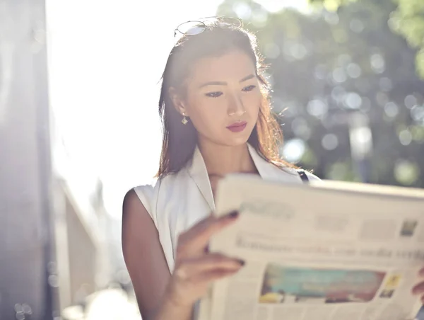 Elegant Asian woman reading a newspaper on the street in the city on a sunny day.