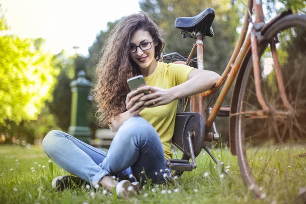 Молодая Женщина Очках Велосипеде Сидит Парке Проверяет Свой Смартфон — стоковое фото