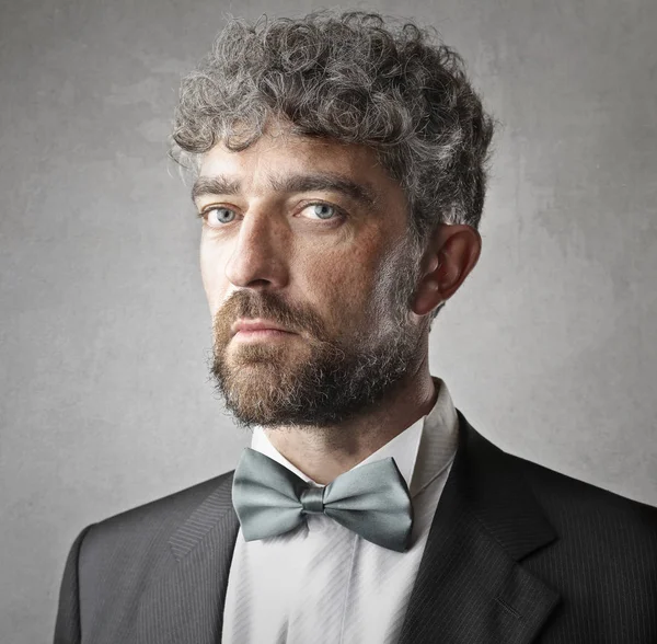 Businessman with beard and bow-tie looking seriously into the camera.