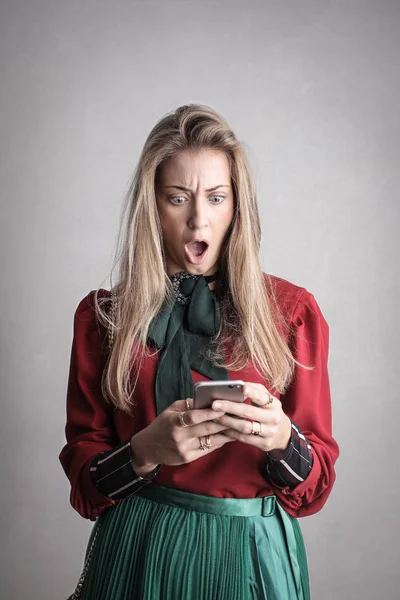 Young blonde woman terrified when checking her smartphone.