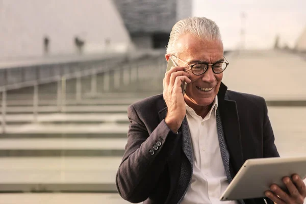 Senior Encantador Hombre Negocios Hablando Teléfono Inteligente Revisando Tableta Ciudad —  Fotos de Stock