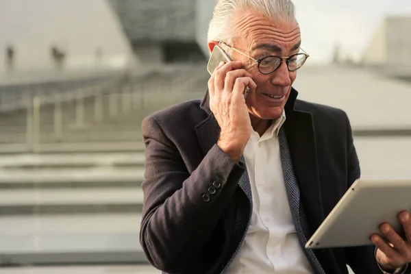 Anciano Hombre Negocios Hablando Teléfono Inteligente Revisando Tableta Ciudad —  Fotos de Stock