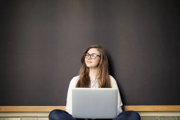 年轻的学生戴着眼镜坐在黑板前与她的笔记本电脑 并想高兴地 — 图库照片