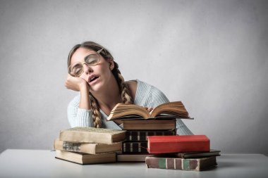 Kitaplarını üzerinde uyku ve yorgun görünümlü gözlüklü genç öğrenci.