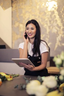 Asyalı kadın tablet ile onun akıllı bir çiçek dükkanında söz.