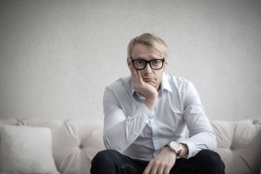 Umutsuzca bir kanepede düşünme gözlüklü sarışın adam. 