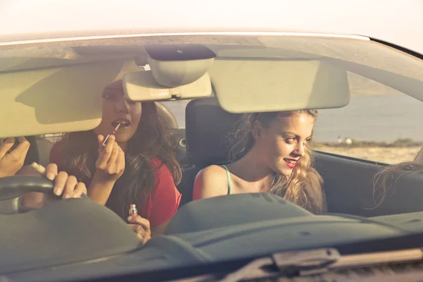 Young women heading to a vacation in their car and adjusting their make-ups.