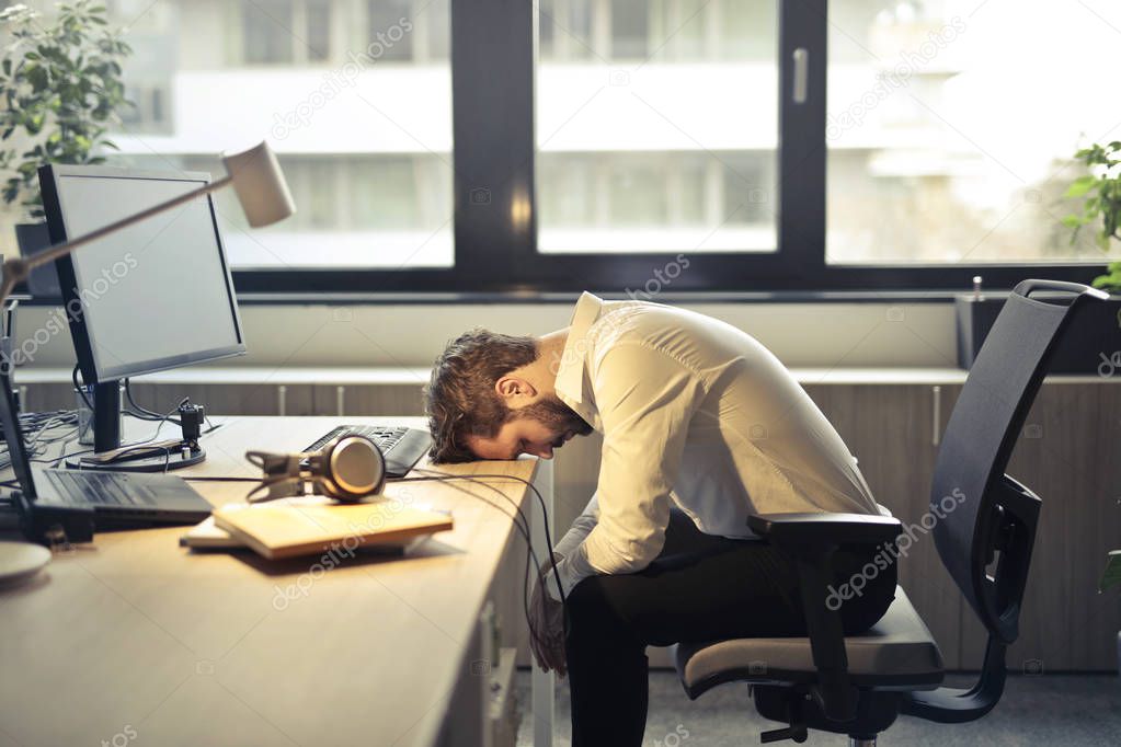Young businessman tired and deprived, feeling lack of sleep at workplace.